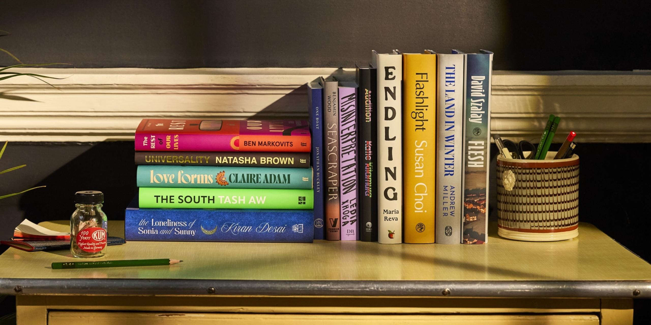 The Booker Prize 2025 longlist of 13 books, displayed artfully on a desk