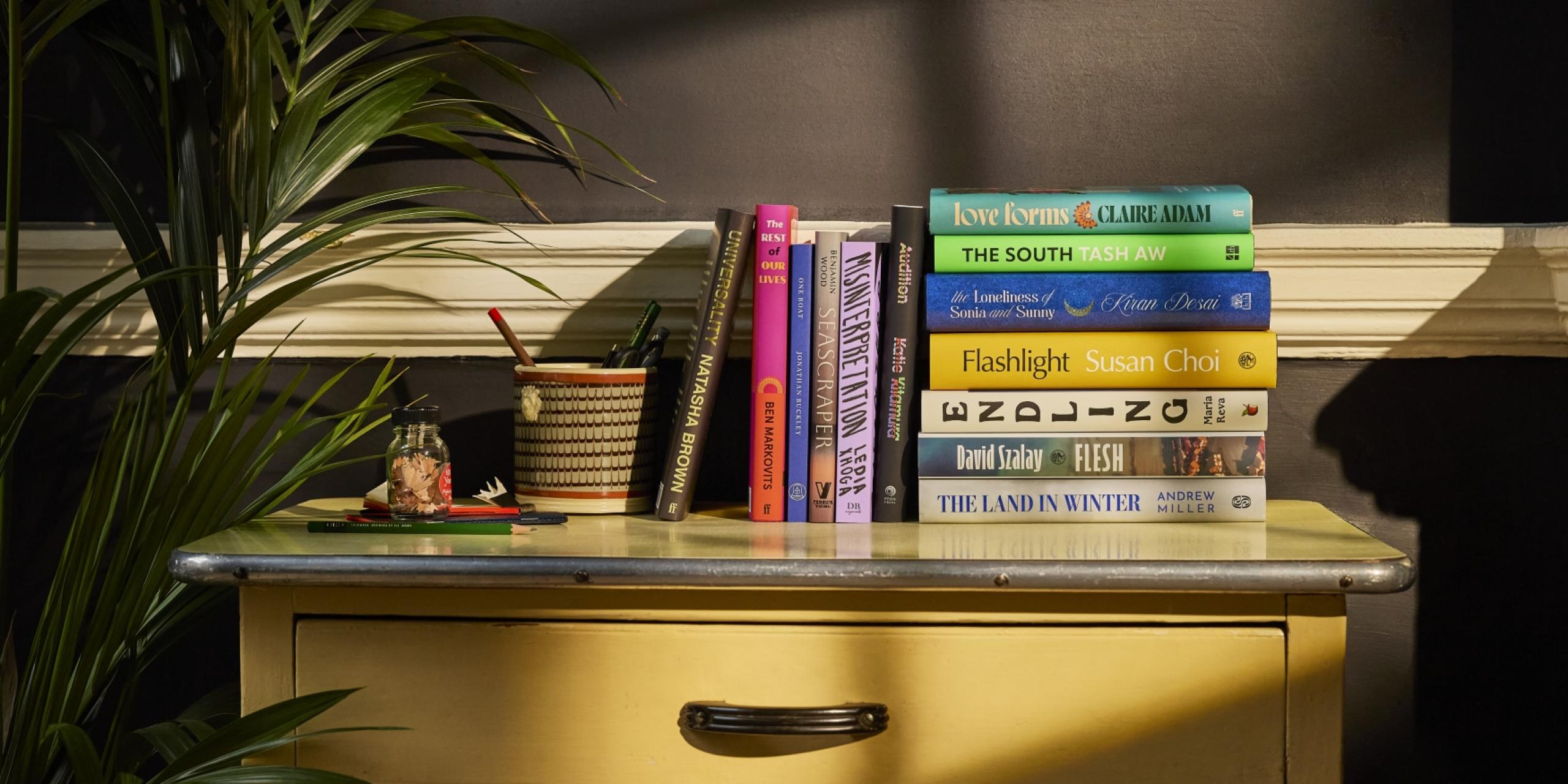 The Booker Prize 2025 longlist of 13 books, displayed artfully on a desk