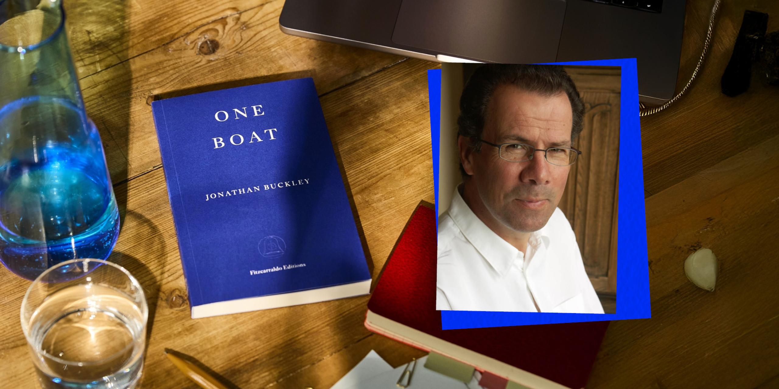 One Boat is on a wood desk with a water jug and glass alongside a photo of Jonathan Buckley