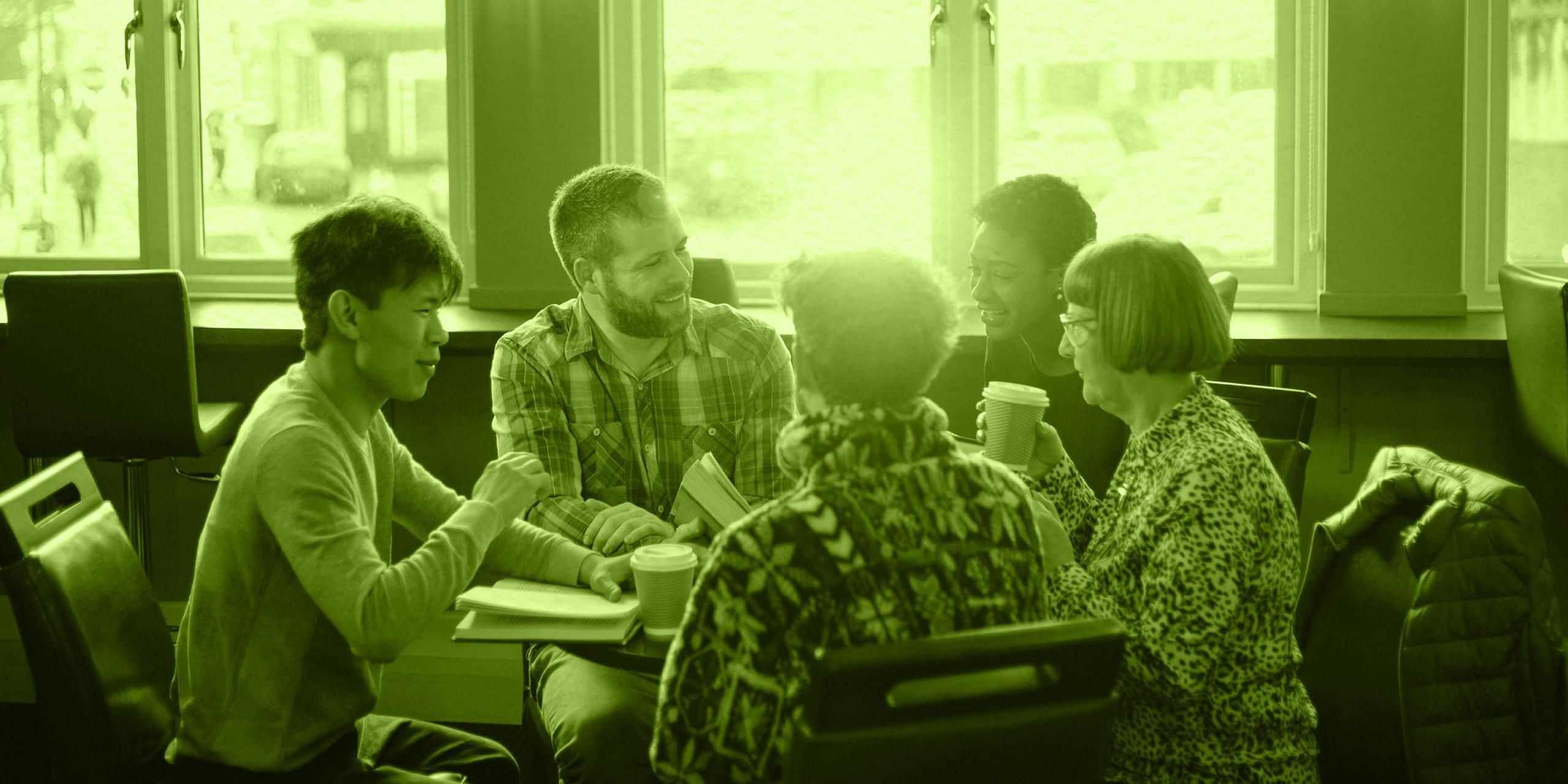 A group of people sitting around a table with coffee cups in their hands and books on the table