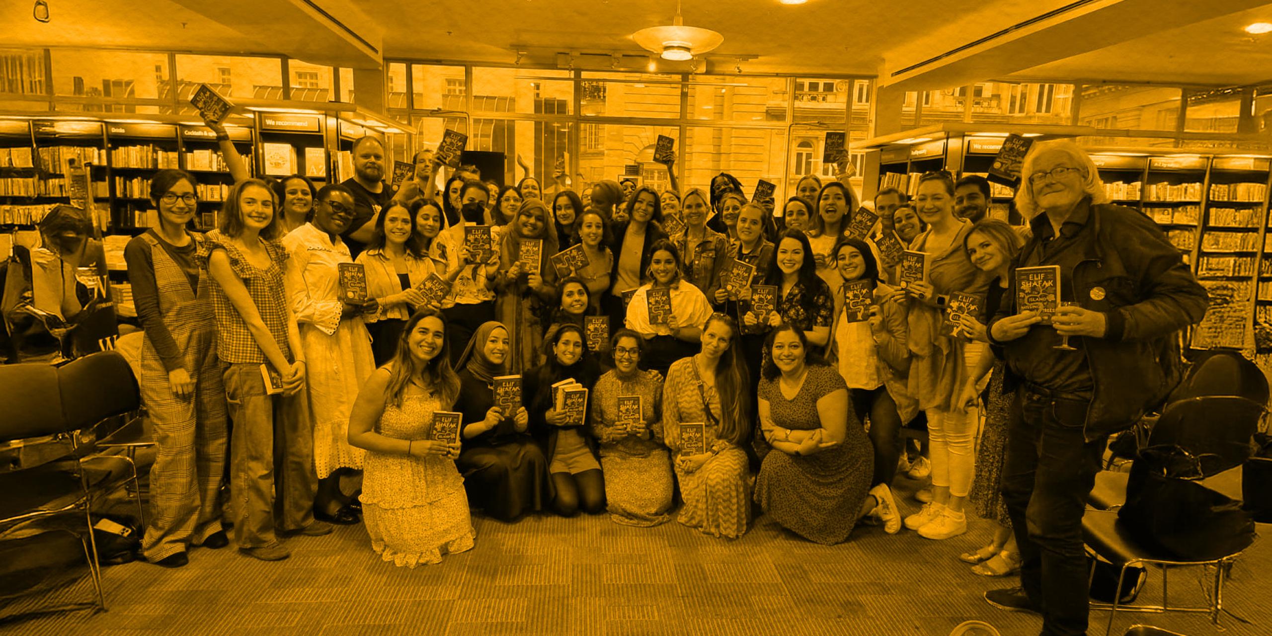 A large group of people pose for a photo holding copies of the same book