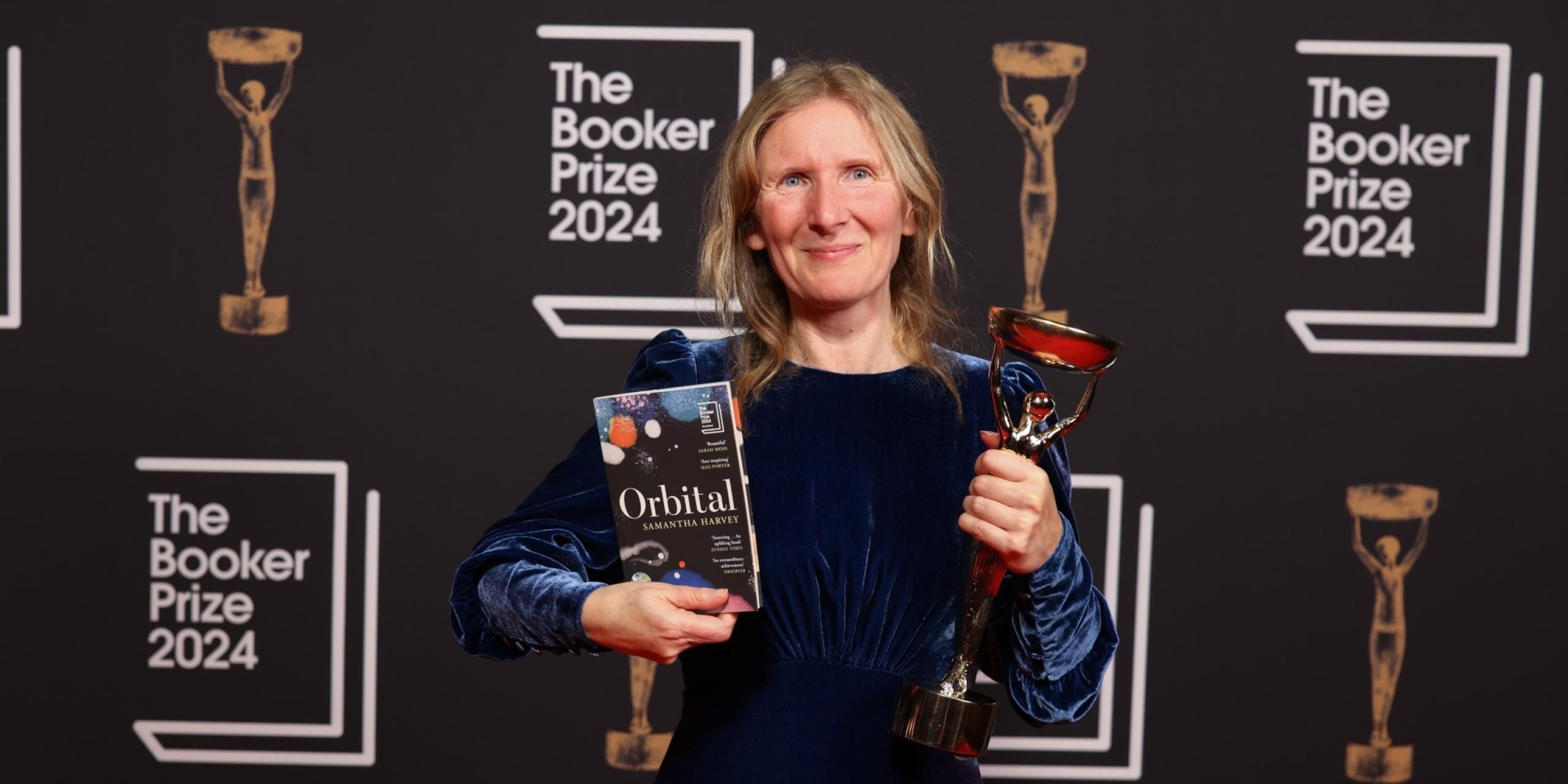 Samantha Harvey holding a copy of her novel, Orbital, and the Booker Prize 2024 trophy