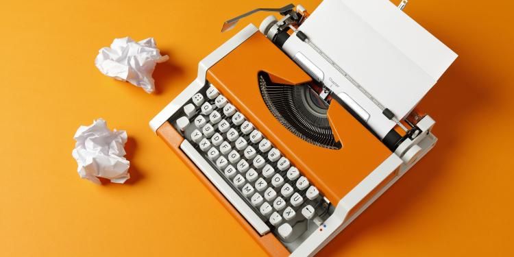 70s typewriter with crumpled paper balls on orange background.